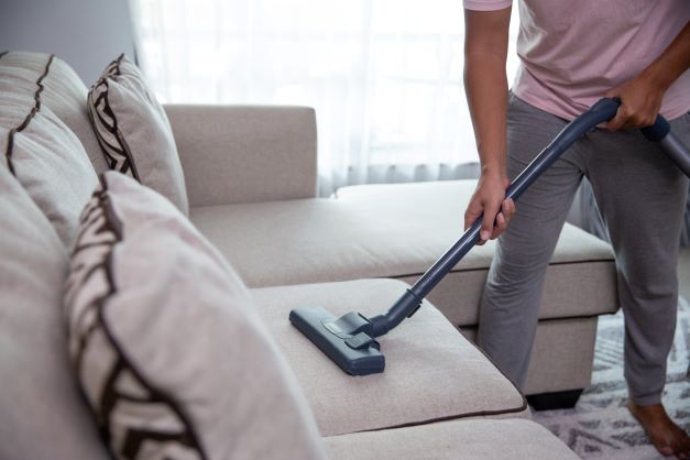 A man vacuuming a couch