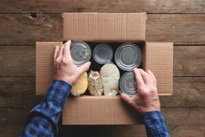 Hands over cardboard box with canned and bagged food
