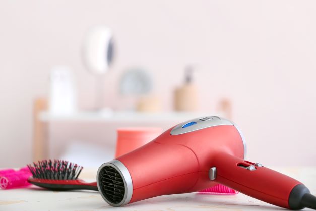 Red blow dryer on counter next to hair brush