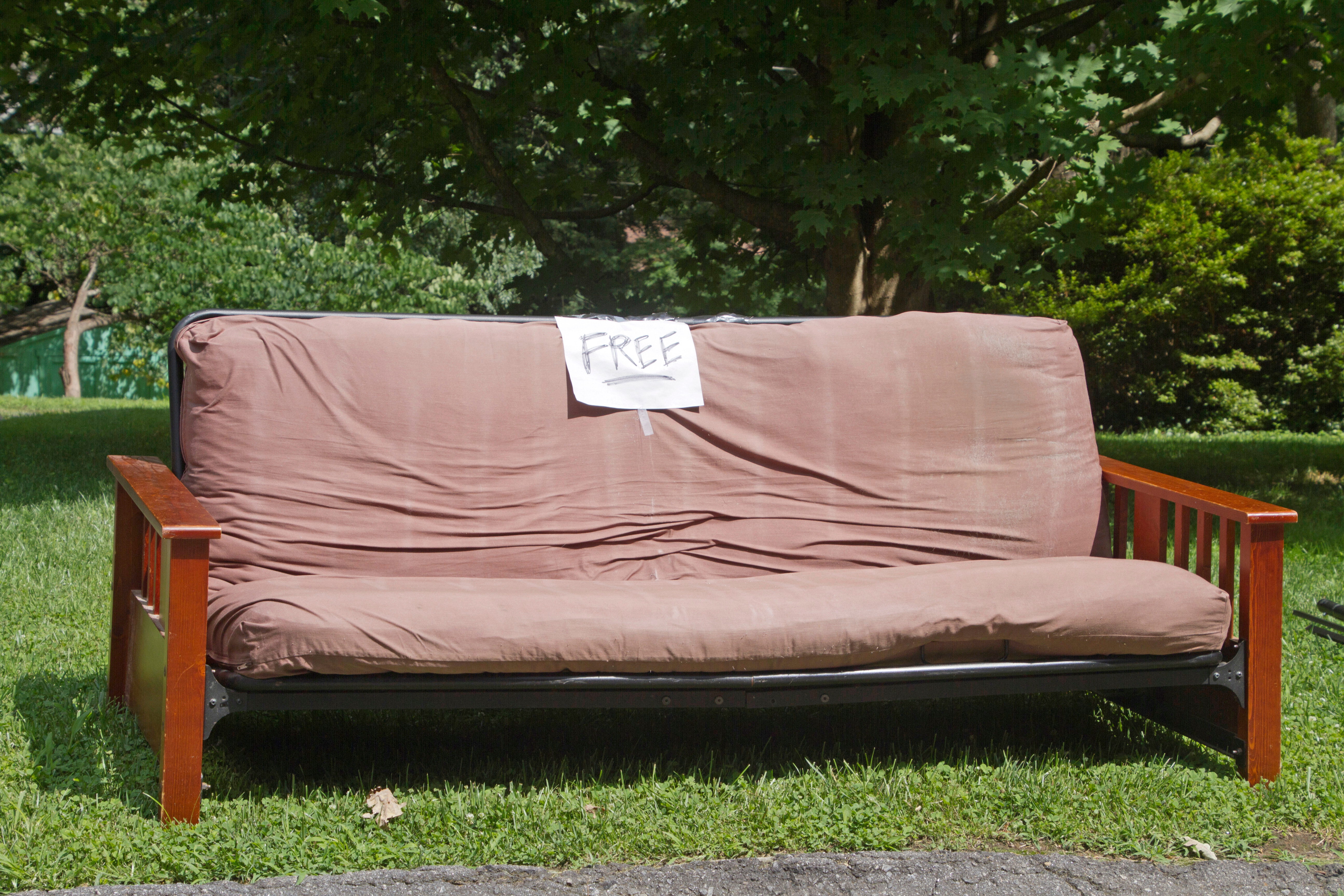 A used futon couch or bed with a free sign left by the street curb to be given away