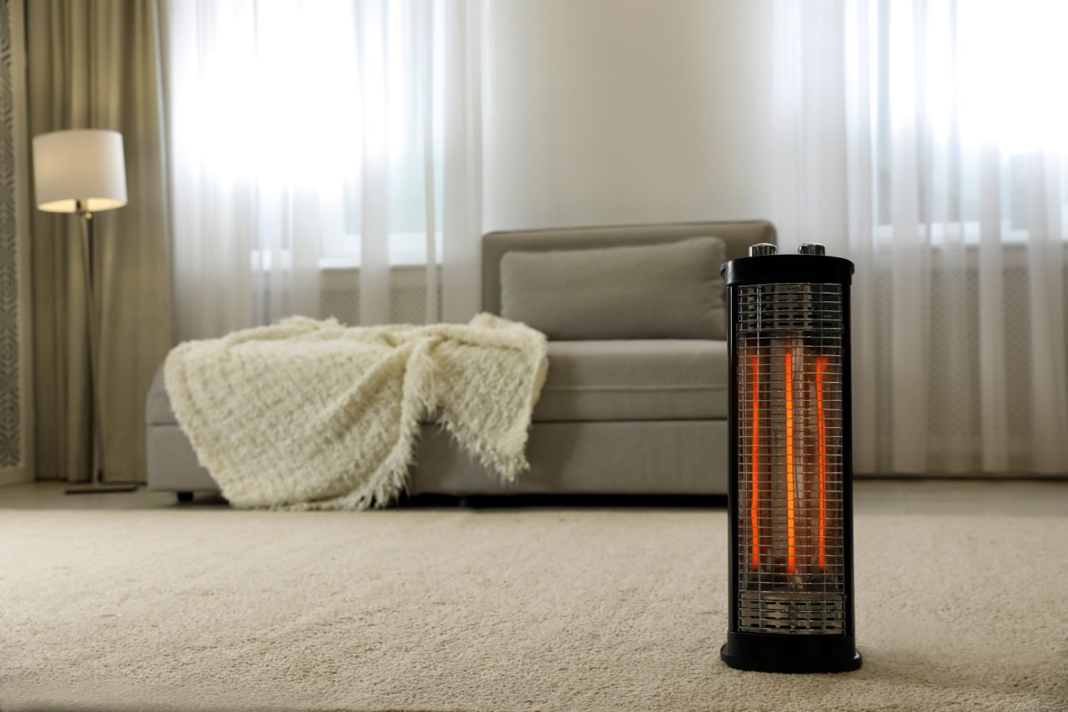Small space heater in a large living room, in front of a couch with a blanket on it