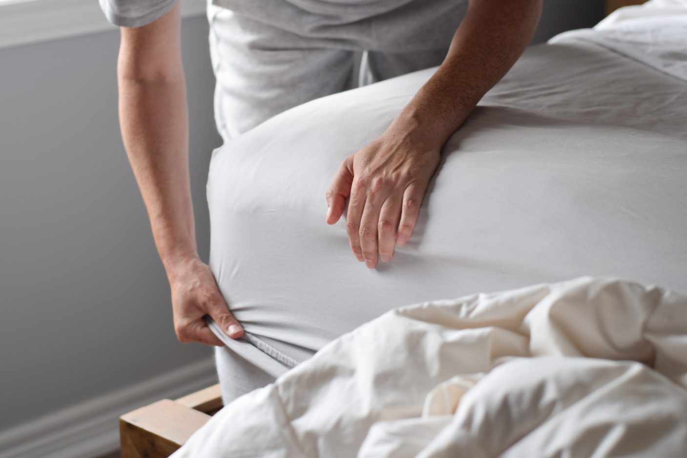 A man is pulling the corner of a fitted bed sheet over the mattress